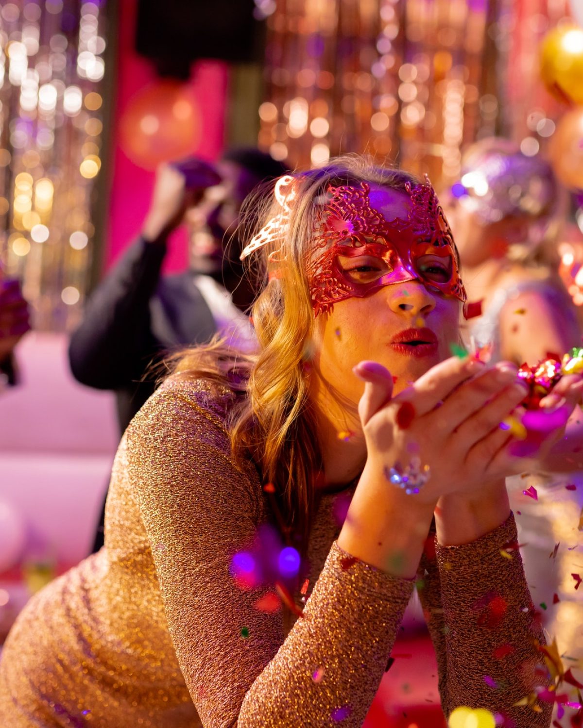 Happy caucasian woman in mask blowing glitter on the dancefloor at a party in a nightclub